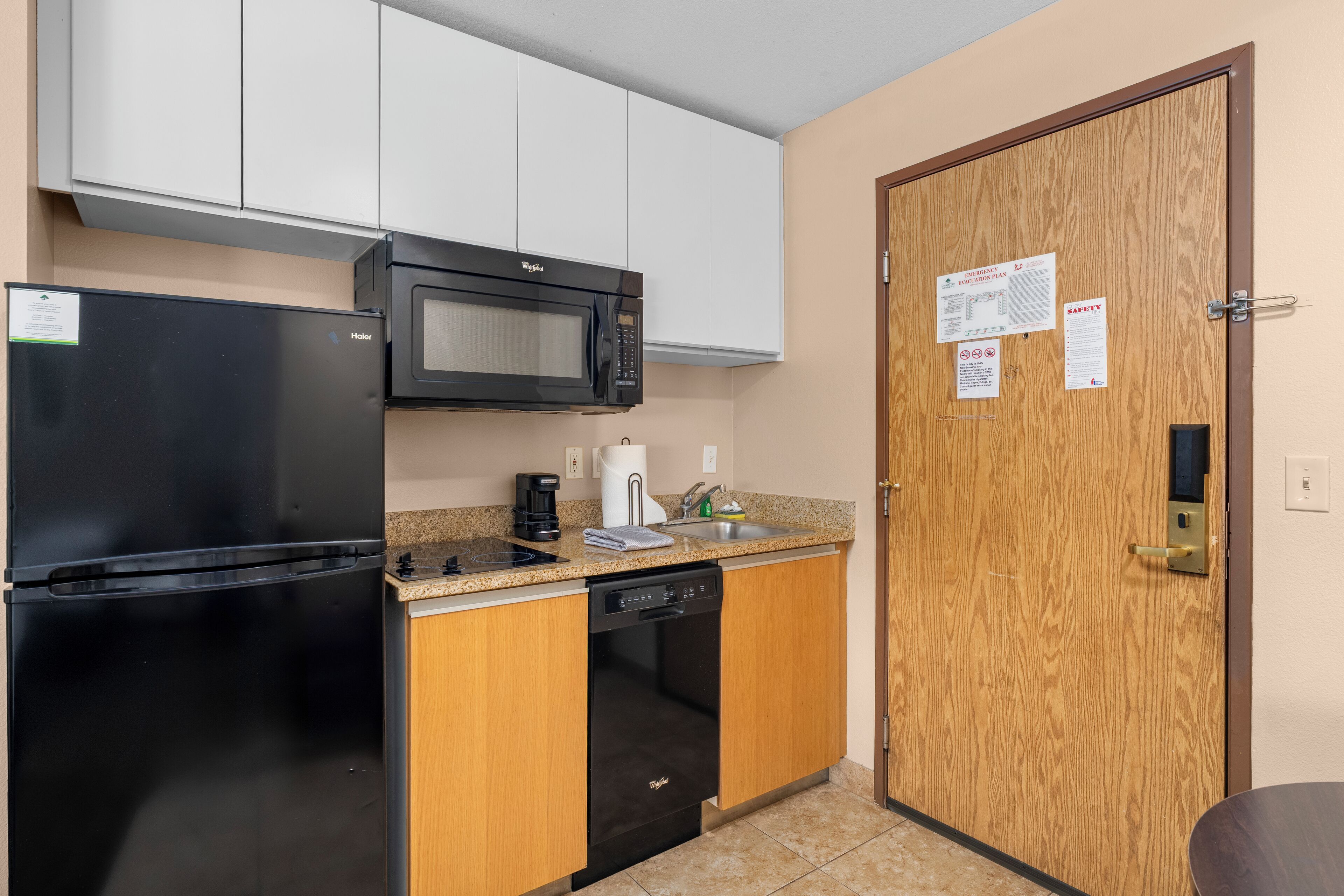 A compact kitchenette with a black refrigerator, a microwave, a coffee maker, and a dishwasher.
