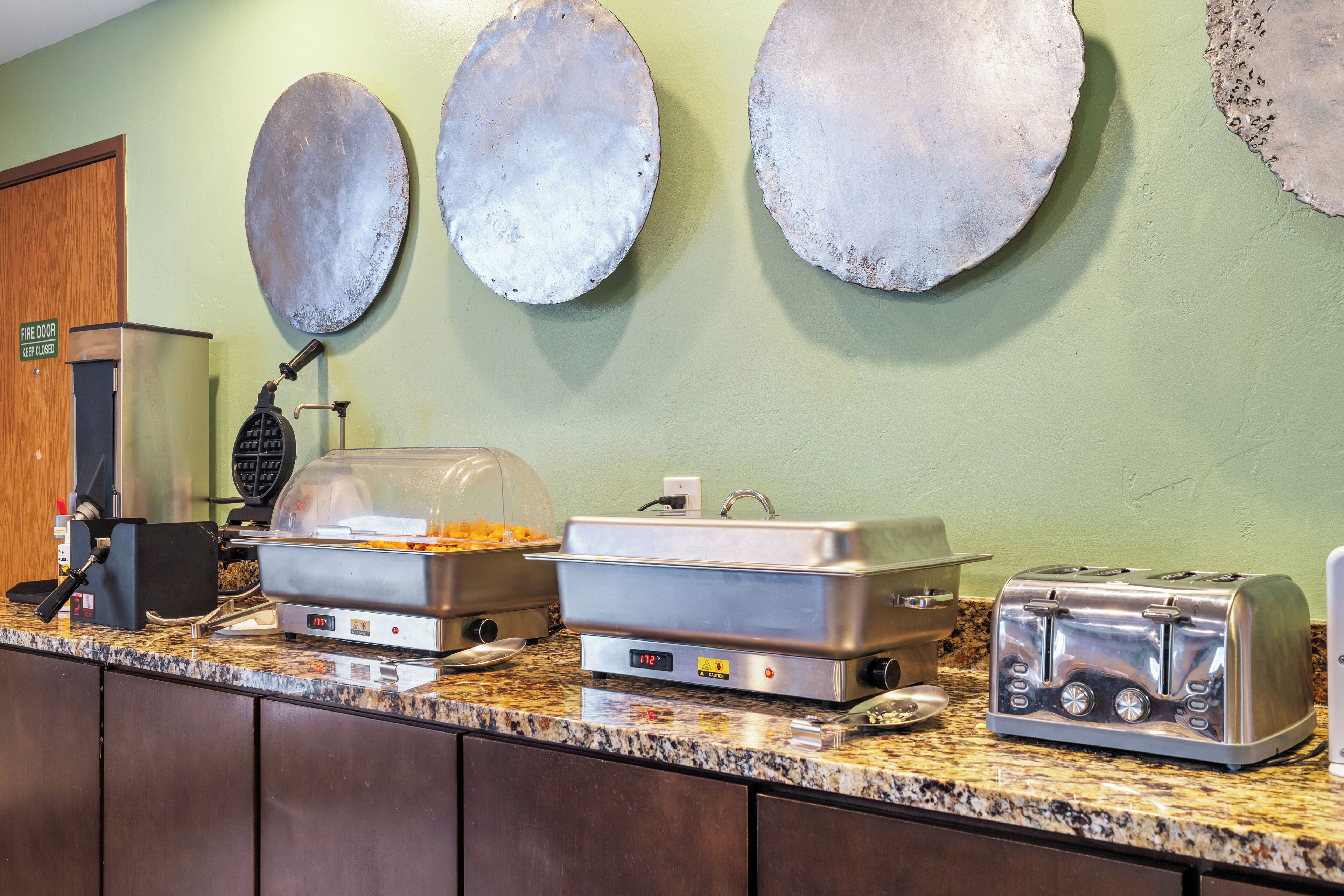 A buffet setup with a toaster, a waffle maker, and a covered food display.