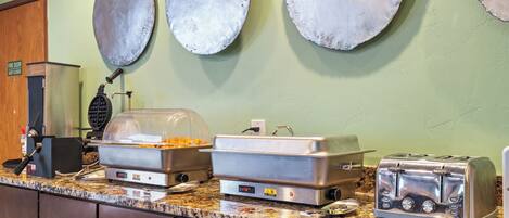 A buffet setup with a toaster, a waffle maker, and a covered food display.