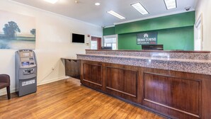 A reception desk with a green wall, a mounted television, and an ATM machine. - HomeTowne Studios by Red Roof Orlando - Casselberry (Casselberry)