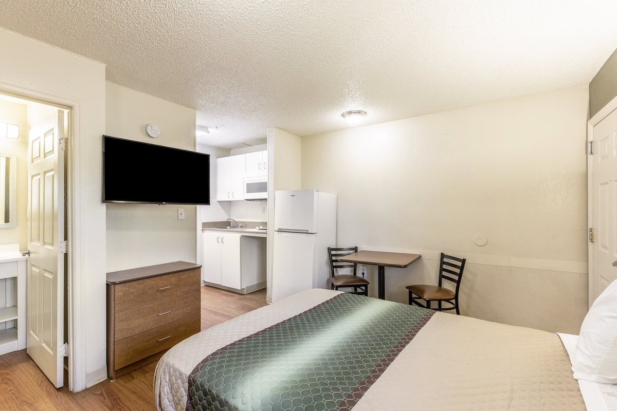 Une chambre d’hôtel compacte comprenant un lit, un téléviseur fixé au mur, une kitchenette et un petit coin repas.