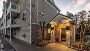 A multi-story hotel with a stone facade entrance, a balcony on the left, and a sign indicating the address '210'. - HomeTowne Studios by Red Roof Orlando - Casselberry (Casselberry)