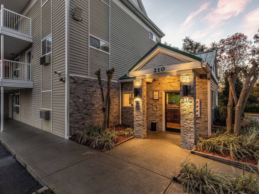 A multi-story hotel with a stone facade entrance, a balcony on the left, and a sign indicating the address '210'.