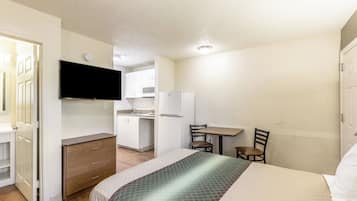Una habitación de hotel compacta con cama, una kitchenette pequeña, televisión y zona de comedor.
