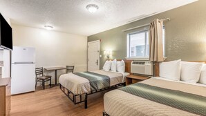 A compact hotel room with a kitchenette, a single bed, a second bed, a desk, and a chair. - HomeTowne Studios by Red Roof Orlando - Casselberry (Casselberry)
