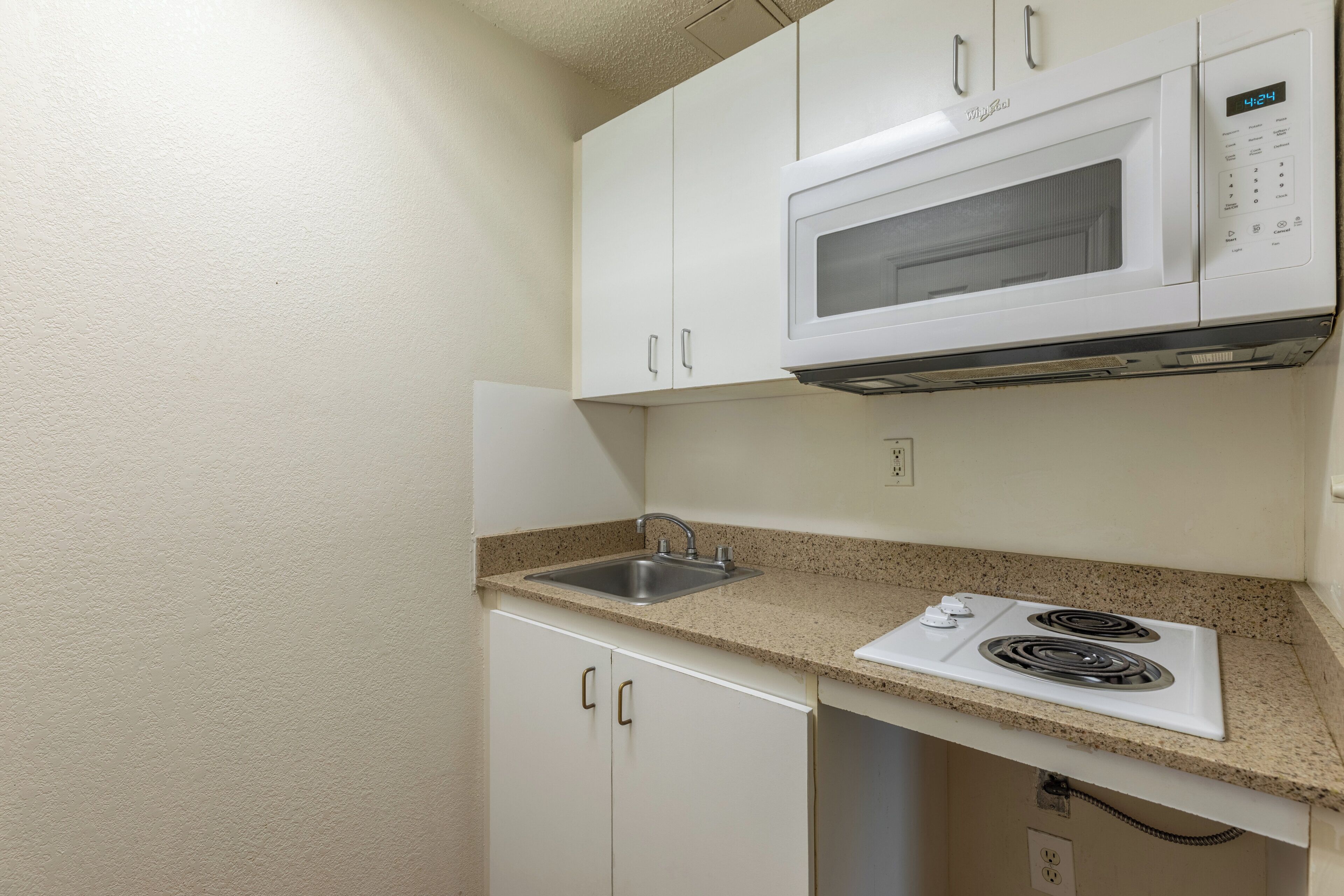 A compact kitchen with white cabinets, a microwave, a sink, and a stove.