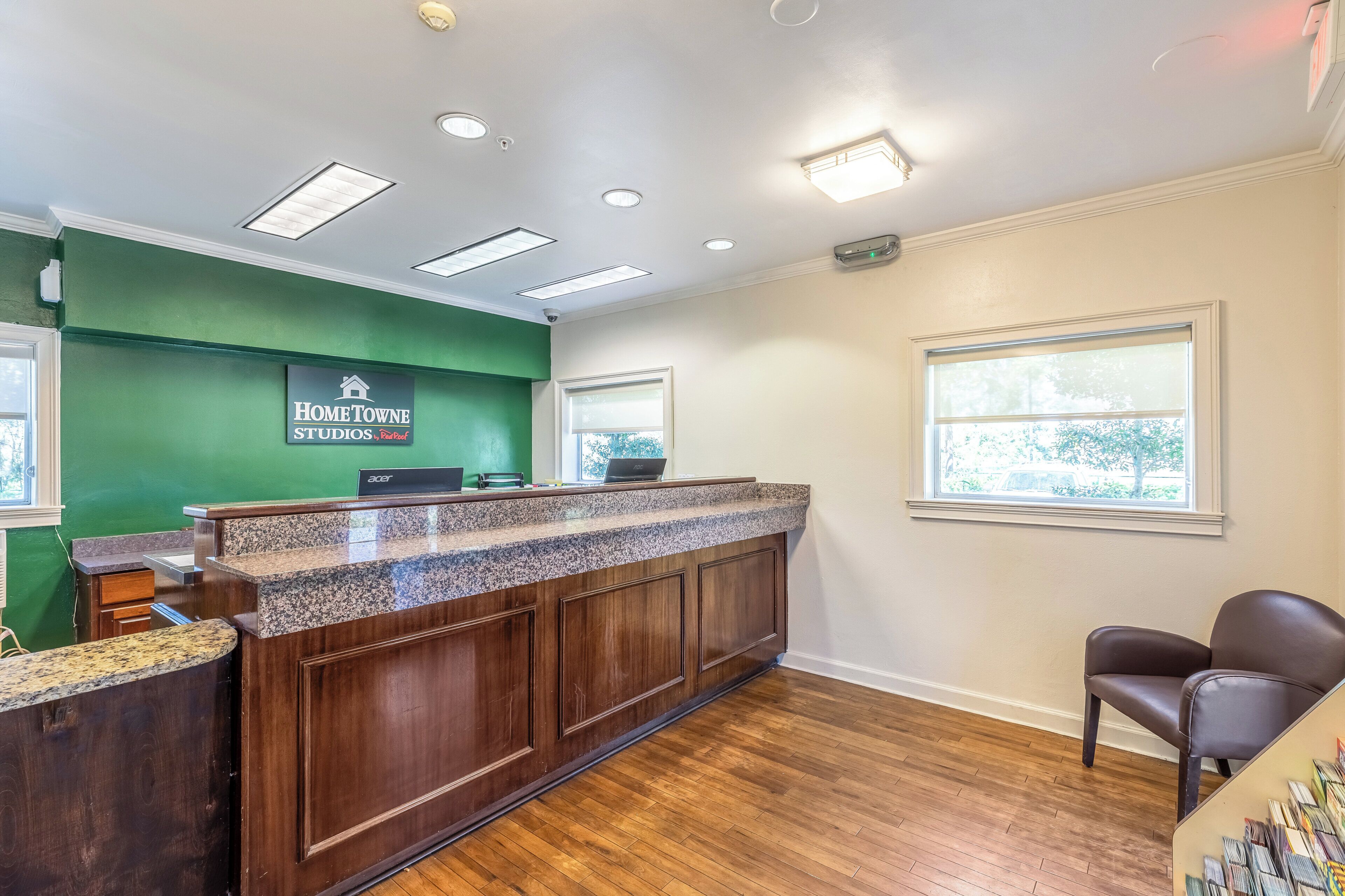 A reception desk with a green wall, wooden paneling, and a window with blinds.