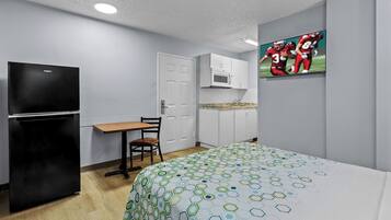 A compact hotel room with a bed, a small kitchenette, a TV, and a desk.
