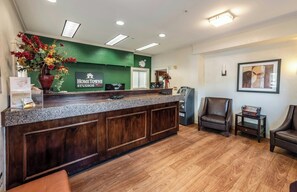 A reception area with a green wall, a wooden reception desk, a clock, and two leather chairs.