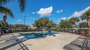A swimming pool with a metal ladder, lounge chairs, and palm trees.