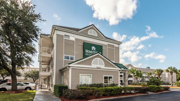 A two-story hotel with a sign reading 'HomeTown Suites.' It features a balcony on the second floor, a green roof, and a number '9435' on the facade.