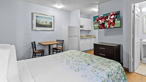 A hotel room with a bed, a desk, a chair, a TV, a microwave, and a refrigerator.
