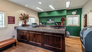 A reception desk with a green wall, a clock, and a sign for HomeTowne Studios. - HomeTowne Studios by Red Roof Orlando South (Orlando)