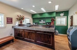 A reception desk with a green wall, a clock, and a sign for HomeTowne Studios. - HomeTowne Studios by Red Roof Orlando South (Orlando)
