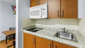 A kitchen with wooden cabinets, a white microwave, a granite countertop, and a stainless steel sink. - HomeTowne Studios by Red Roof Orlando South (Orlando)