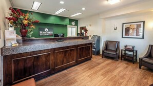 A reception area with a green wall, a wooden reception desk, a clock, and two leather chairs.