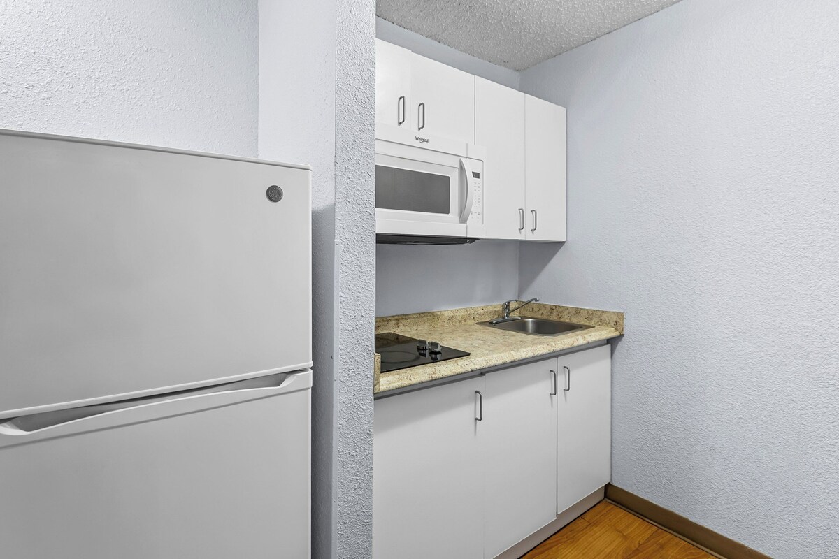 A compact kitchen with white cabinets, a built-in microwave, and a granite countertop.