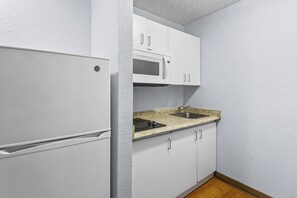 A compact kitchen with white cabinets, a built-in microwave, and a granite countertop. - HomeTowne Studios by Red Roof Orlando South (Orlando)