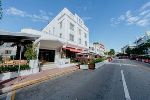 A white building with a red awning, outdoor seating, and potted plants. - Viajero Miami (Miami Beach)