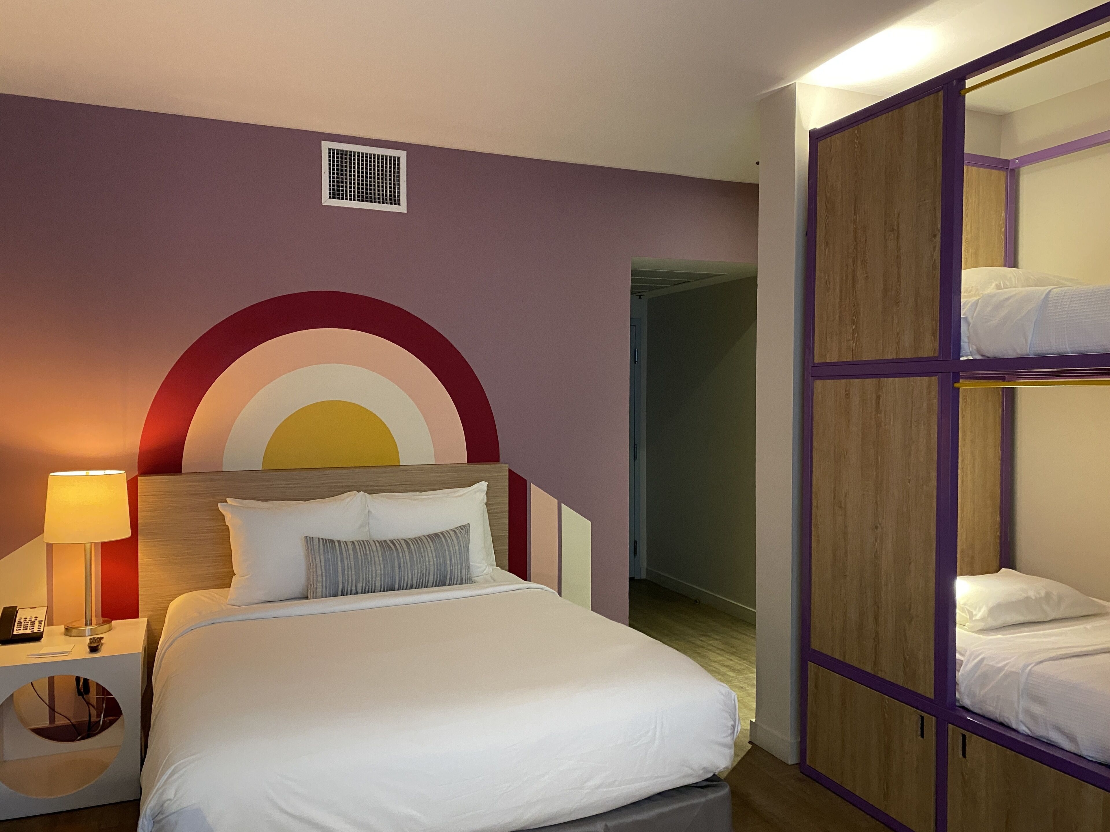A hotel room with a bed, bedside table, lamp, and a wardrobe with two beds.