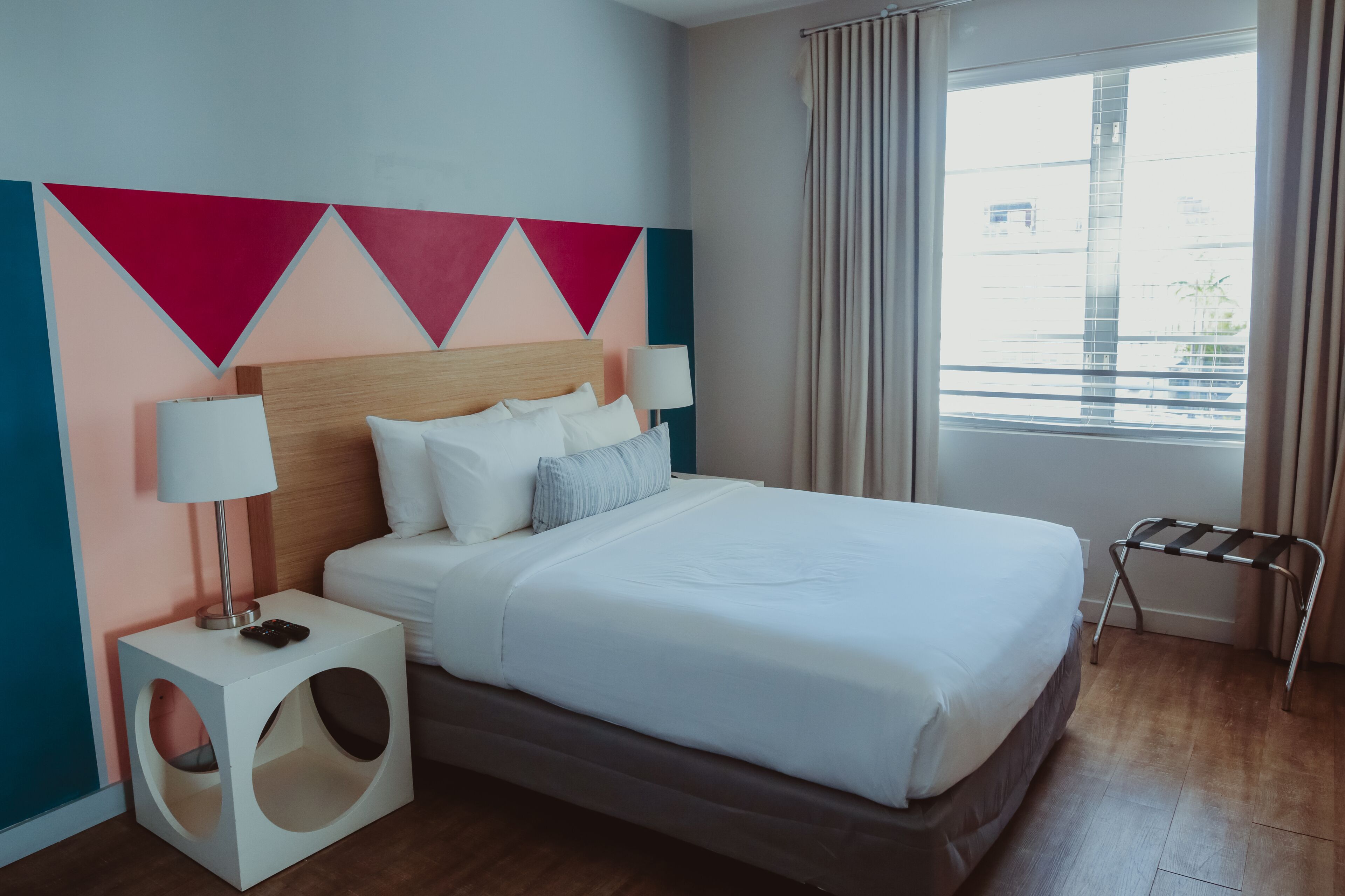 A modern hotel room with a large bed, a side table with a lamp, and a window with curtains.