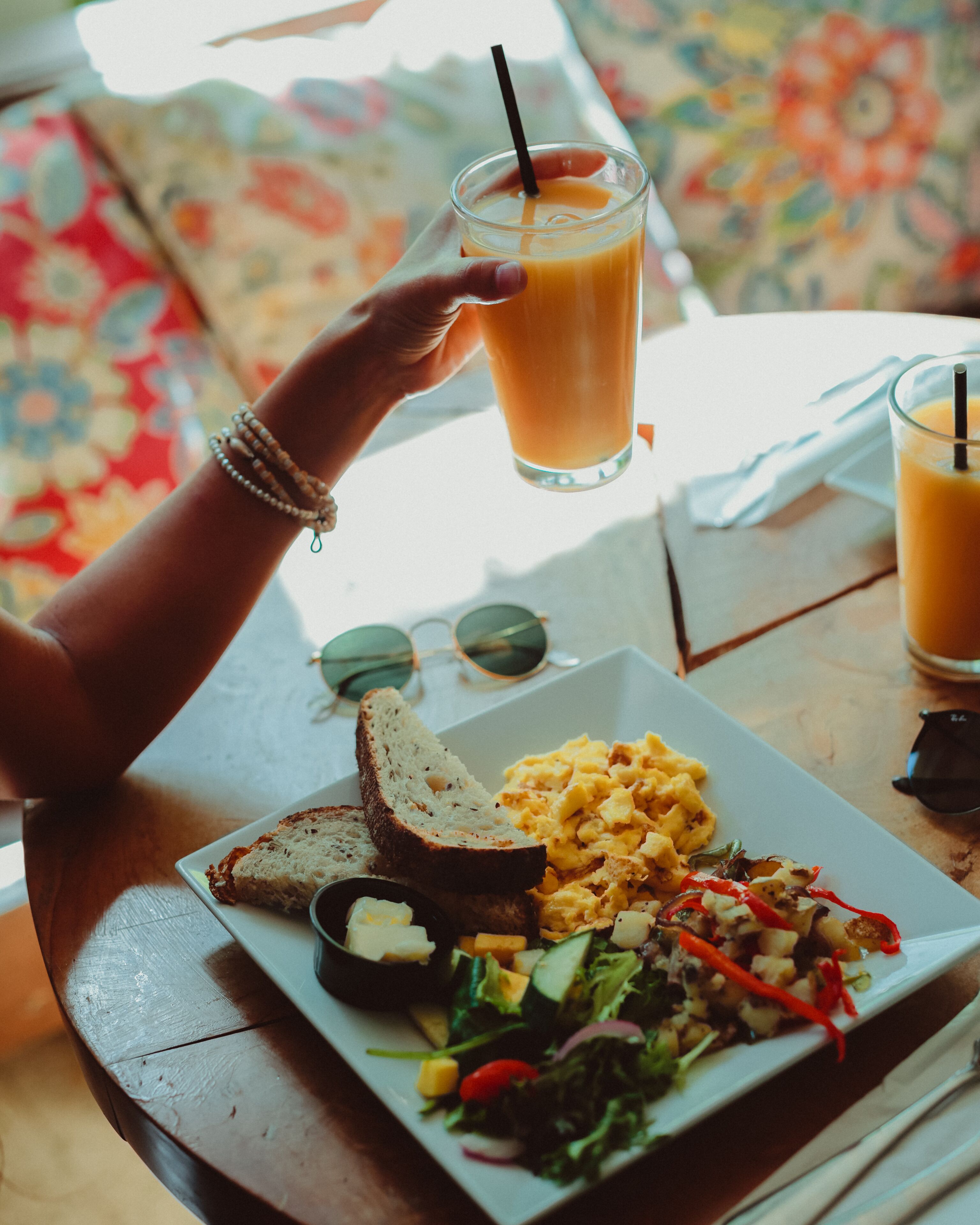 A meal with toast, scrambled eggs, and a salad, and a glass of orange juice on a table.
