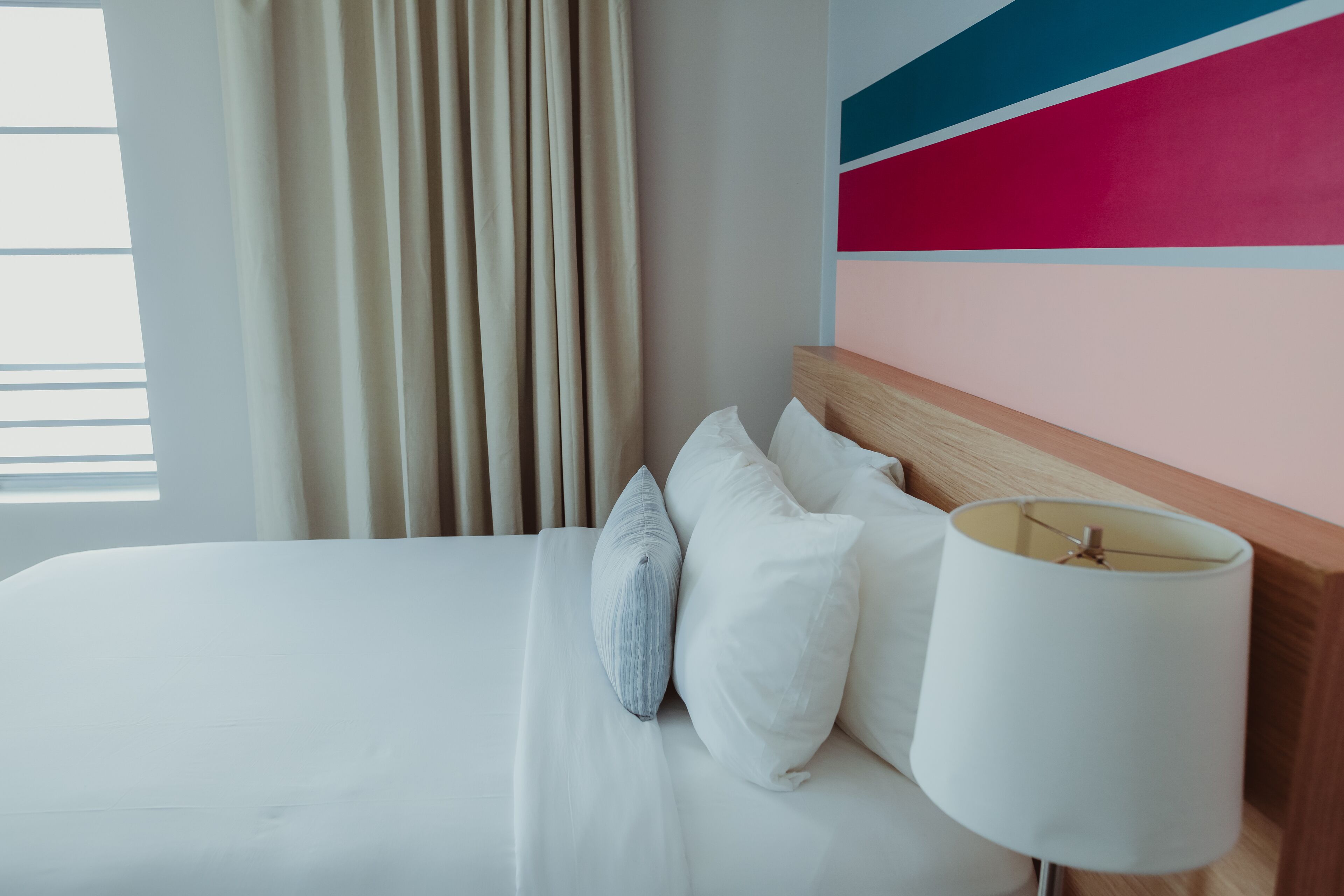 A hotel room with a bed, pillows, a lamp, and a colorful wall.