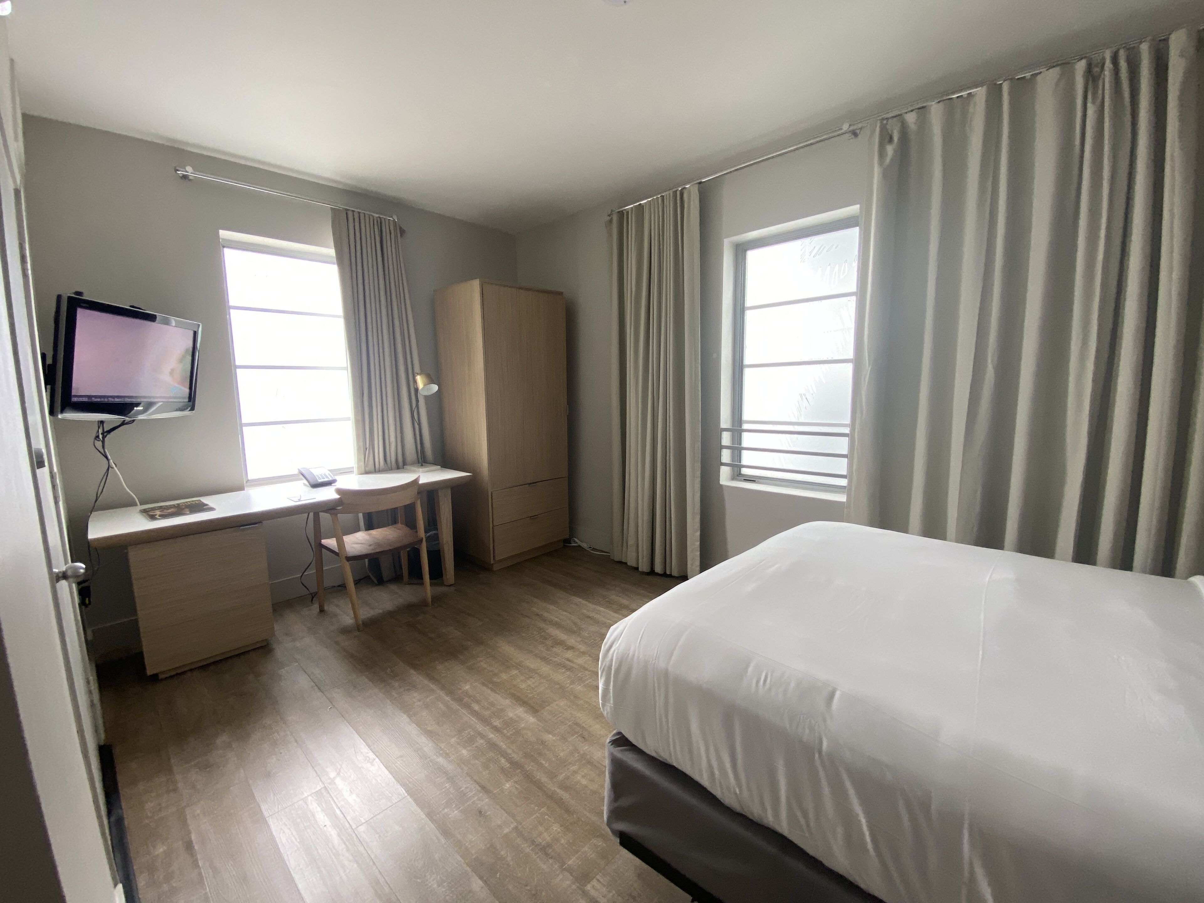 A hotel room with a bed, a desk with a chair, a television, and a wardrobe.