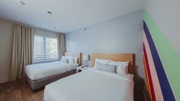 A hotel room with two beds, a window with curtains, a nightstand with a lamp, and a colorful wall decoration.