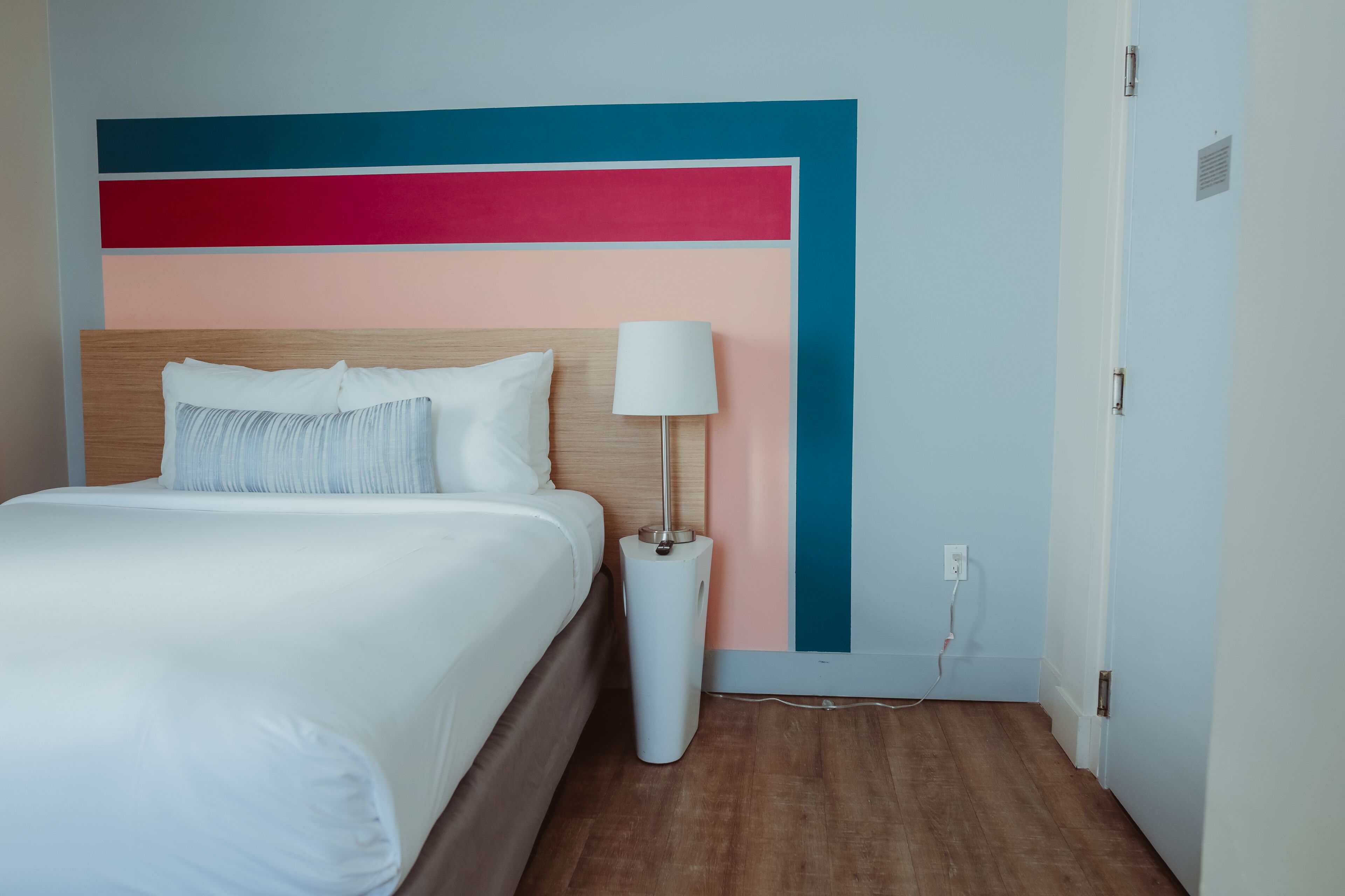 A hotel room with a bed, a bedside lamp, and a wall with a geometric design.