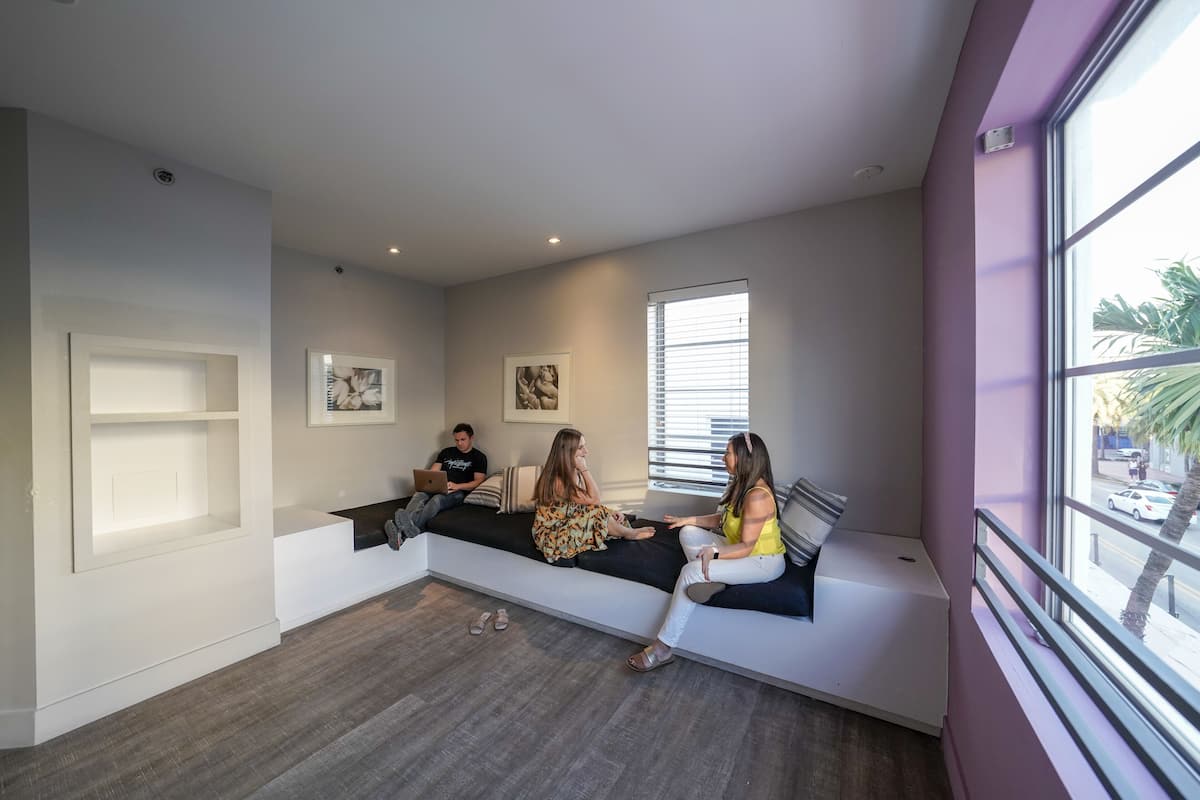 A modern interior with a built-in bench seating area, a large window with blinds, and a visible door.