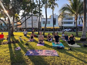 Guests can practice yoga in a serene outdoor setting surrounded by trees and a nearby building.