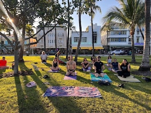 Guests can practice yoga in a serene outdoor setting surrounded by trees and a nearby building.
