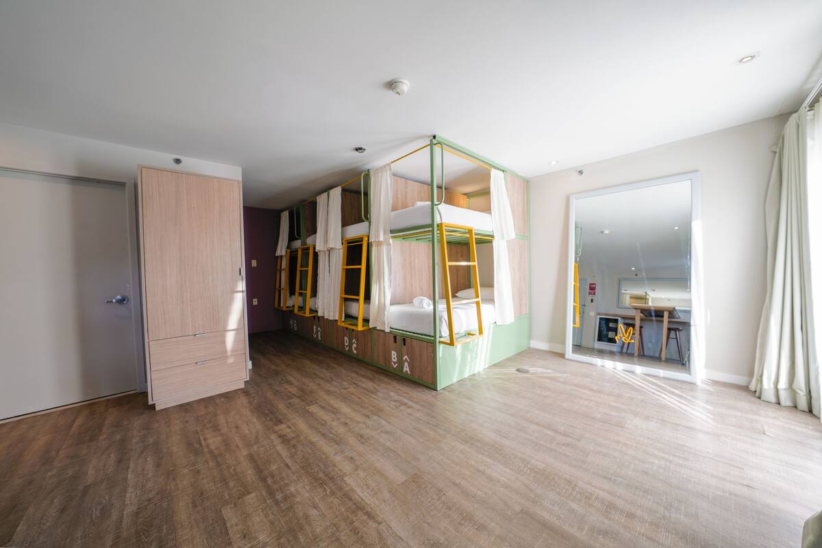 A room with a bunk bed, a wardrobe, and a kitchen area visible through a glass door.