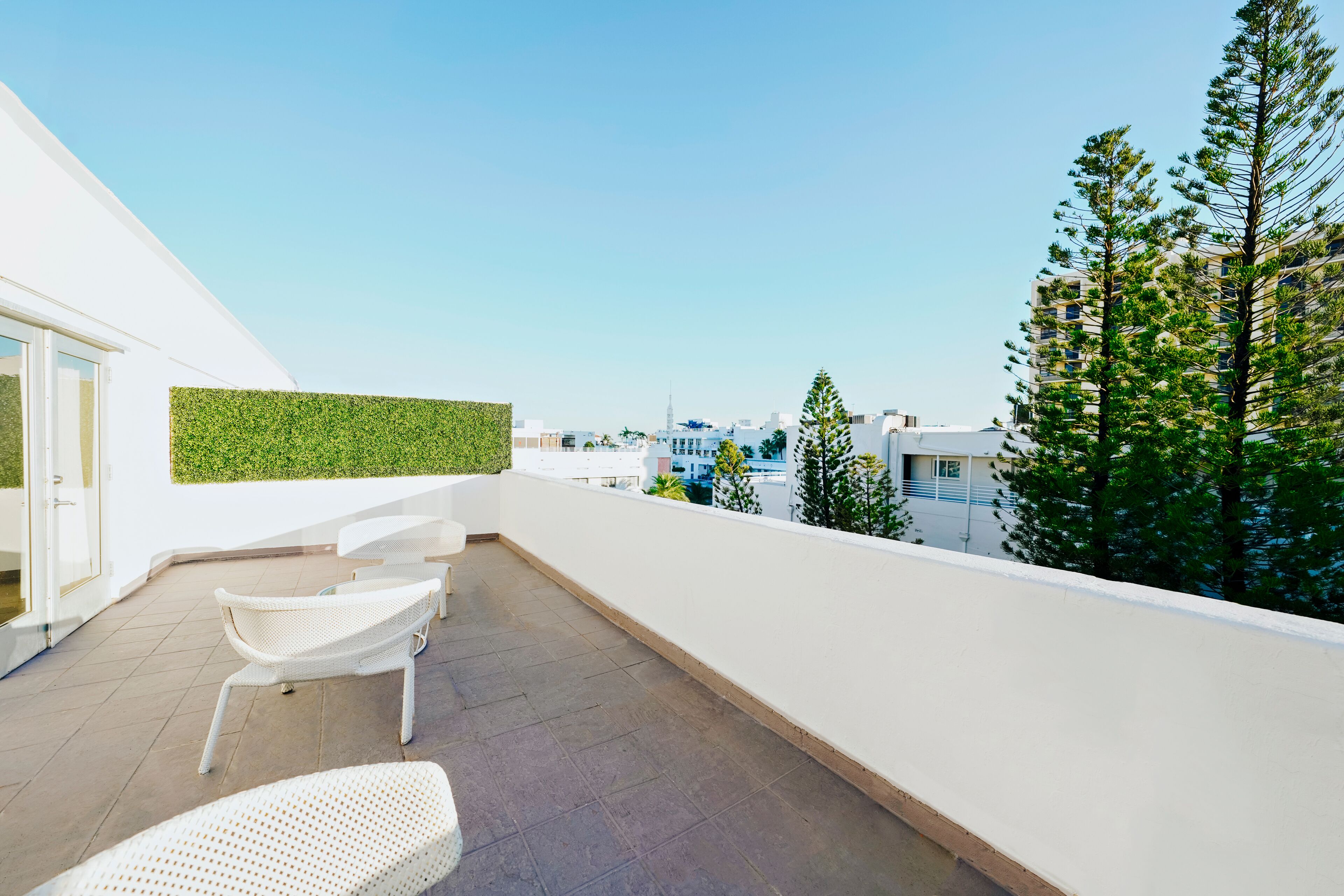 A rooftop terrace with a white chair, a white wall, and a green vertical garden.