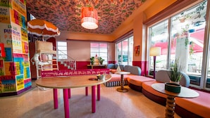 A vibrant hotel lobby with a wooden table, pink chairs, a sofa, and a staircase.
