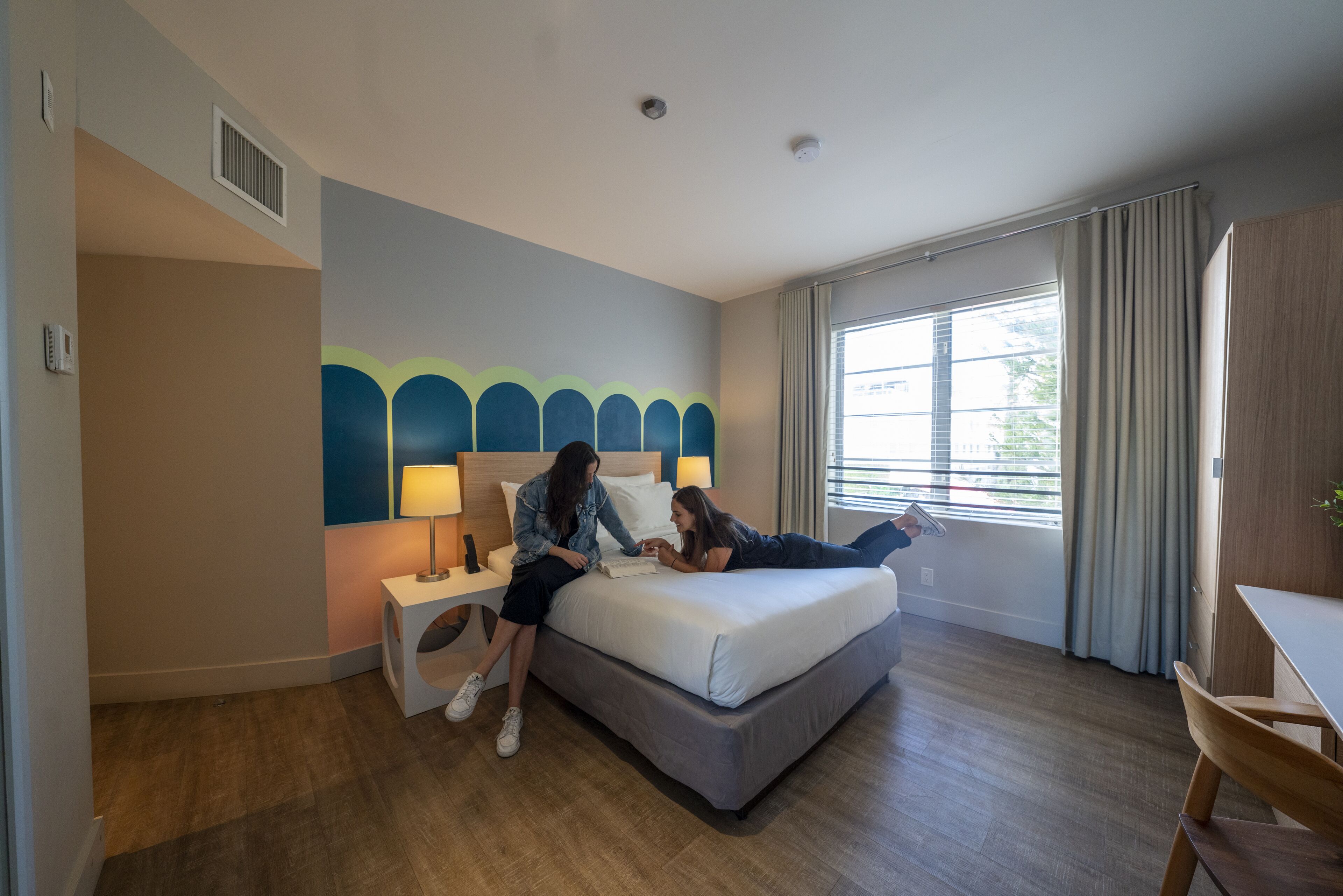 A hotel room with a bed, bedside tables, a lamp, a window with curtains, and a view of the outdoors.