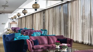 Una habitación amplia con varias zonas de estar, incluyendo sofás y sillones, dispuestos en fila. Hay luces de techo y un ventanal con cortinas.