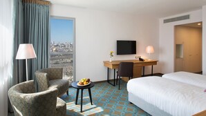 Habitación de hotel con cama, escritorio con silla, televisor y vistas a la ciudad.