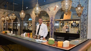 Zona de bar con un barman, una variedad de quesos y botellas de vino.