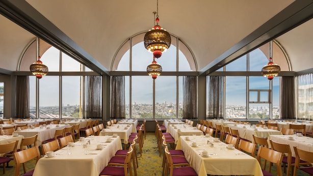 Un comedor con mesas dispuestas para el servicio, ventanas amplias y vistas a la ciudad.