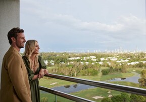 Um casal em frente a uma varanda com vista para um campo de golfe e o horizonte da cidade.