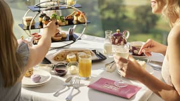 A dining table with a tiered dessert stand, a glass of orange juice, and a pink menu.