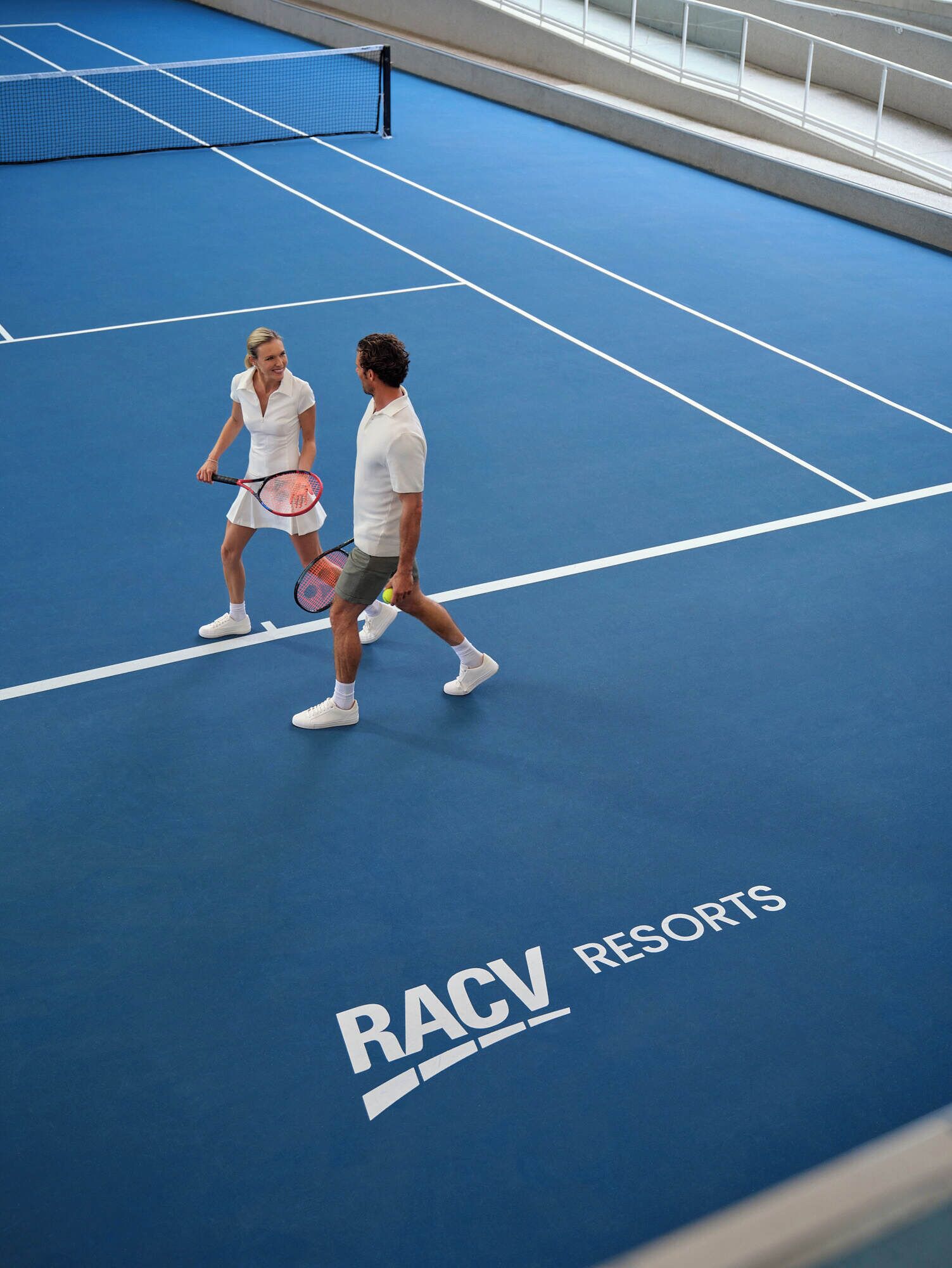 A tennis court with a net, marked lines, and the text "RACV Resorts" on the floor.