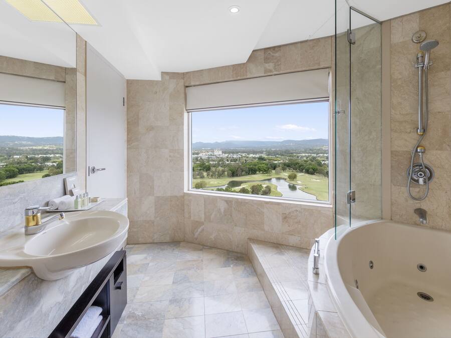 A modern bathroom with a large bathtub, a double sink, and a large window offering a view of a golf course.