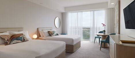 Habitación de hotel con dos camas, un escritorio, una silla, un televisor y un ventanal grande con cortinas.