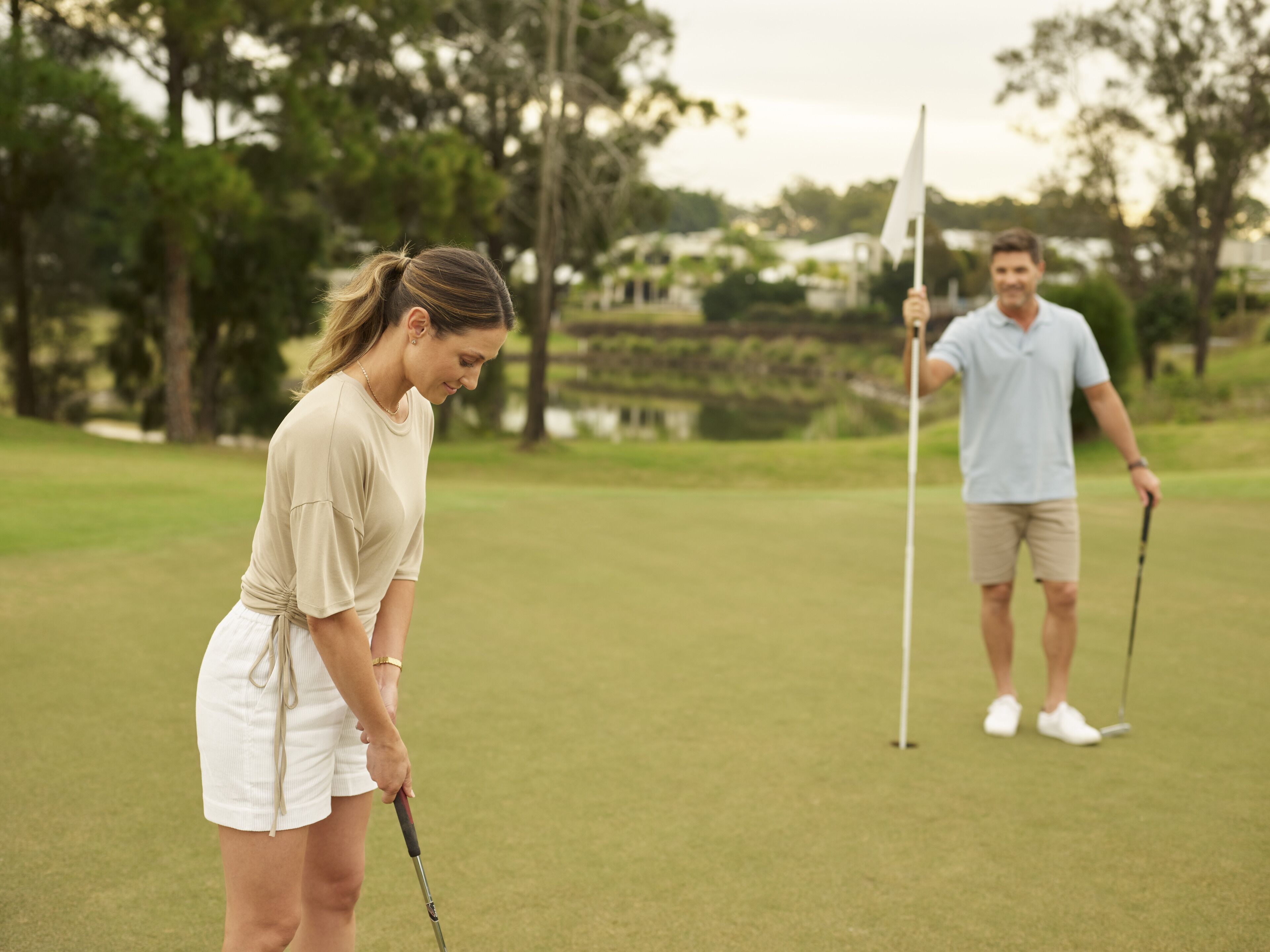 A golf course with a putting green, trees, and a distant building.