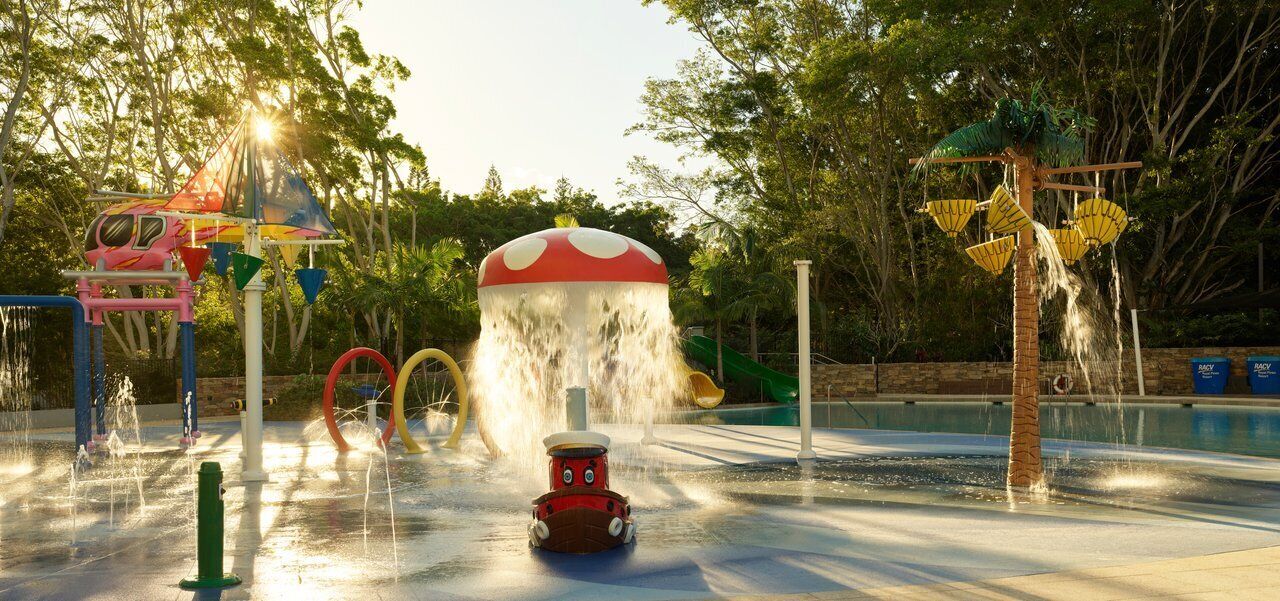 Ein Wasserpark mit einer roten und weißen pilzförmigen Wasserspender, einer Rutsche und einem Spielzug.