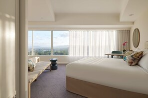 A modern hotel room with a large bed, a bench, a small table, and a view of the city.