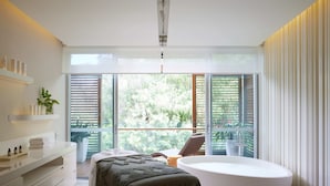Une salle de bain moderne avec une grande baignoire, un meuble-lavabo avec des étagères et une vue sur la verdure grâce à de grandes fenêtres.